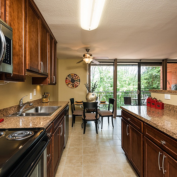 Sophisticated kitchen with rich wood cabinetry and granite countertops leading to a charming dining area with lush garden views.