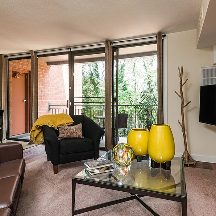 Charming living room with modern decor, featuring vibrant yellow vases, cozy seating, and floor-to-ceiling windows leading to a lush balcony view.