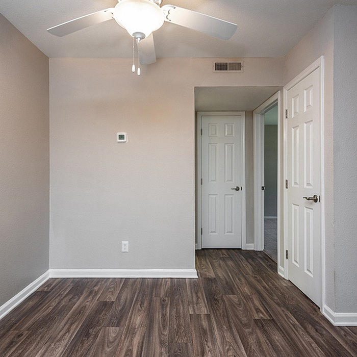 Bright, modern interior with sleek wood flooring, neutral walls, and a ceiling fan, featuring white doors leading to adjacent rooms.