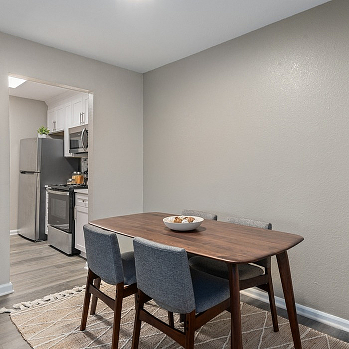 Contemporary dining area with a sleek wooden table, stylish chairs, and a view into a modern kitchen with stainless steel appliances.
