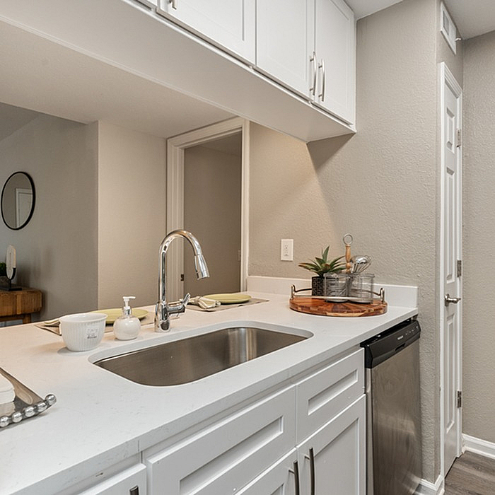 Modern kitchen with elegant white cabinetry, sleek chrome faucet, and a stylish countertop featuring a decorative plant and accessories.
