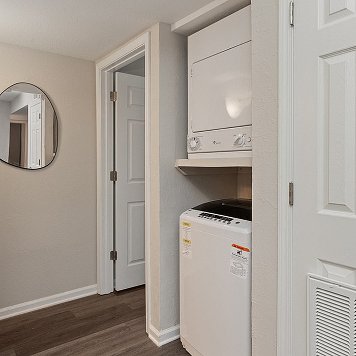 Modern laundry area with stacked washer and dryer, sleek flooring, and stylish mirror in a cozy apartment setting.