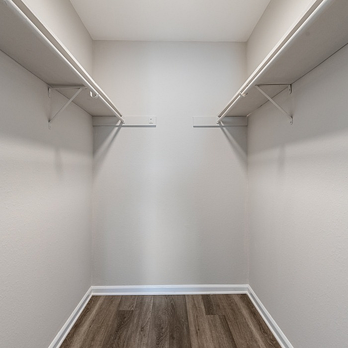 Spacious walk-in closet with sleek shelving and elegant wood-style flooring, offering ample storage room and modern style.