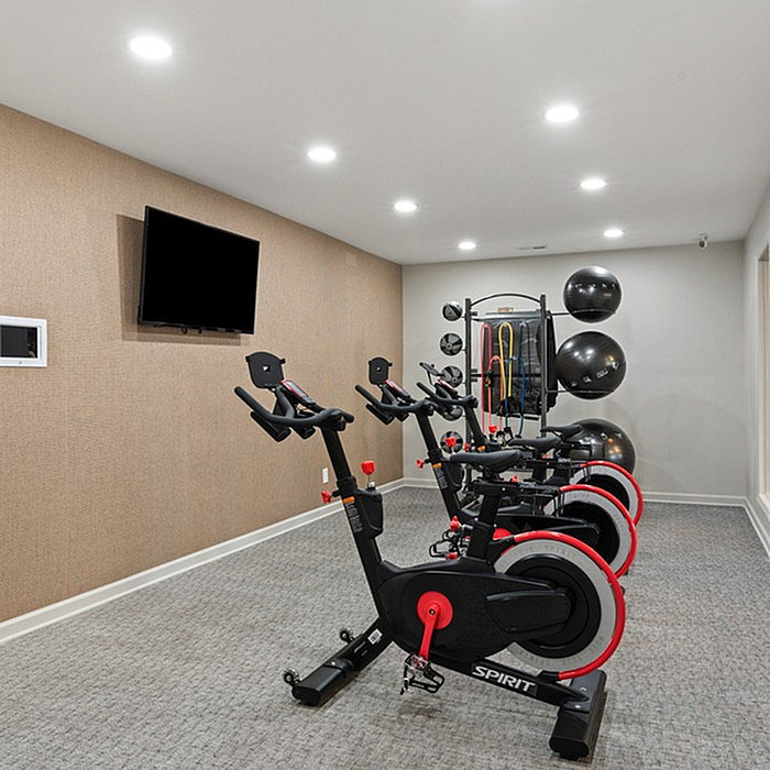 Modern fitness room equipped with stationary bikes, a sleek wall-mounted TV, and versatile exercise gear for a dynamic workout experience.