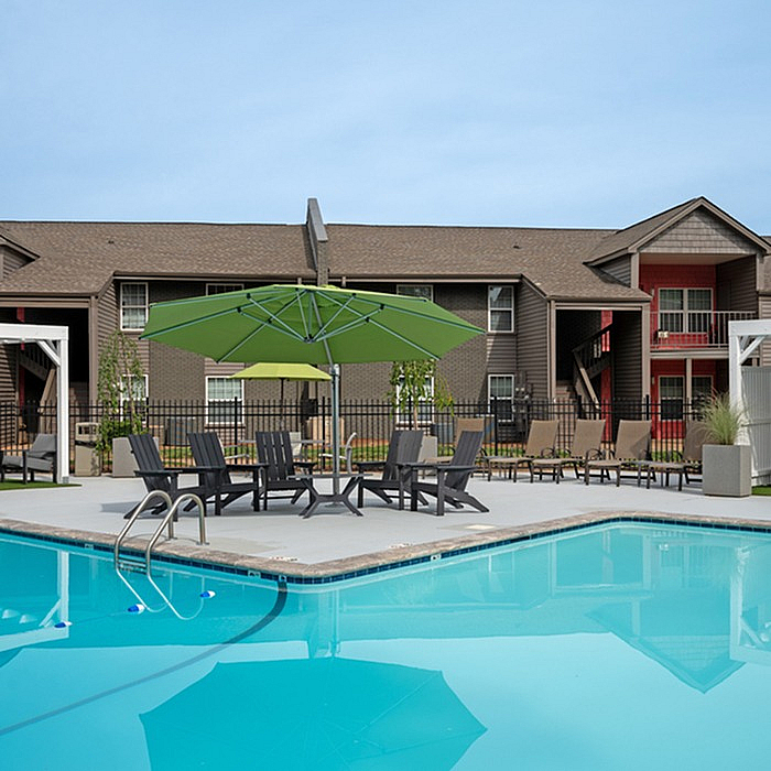 Inviting apartment complex with a sparkling outdoor pool, surrounded by stylish lounge chairs and vibrant green umbrellas.