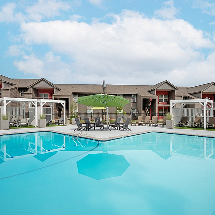 Inviting apartment complex with modern architecture, featuring a sparkling swimming pool, shaded lounge area, and beautifully landscaped surroundings.