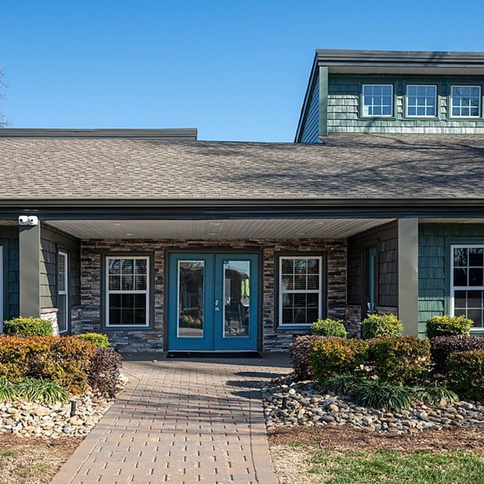 Charming modern house with a blue door, stone facade, and lush landscaping, perfect for welcoming guests.