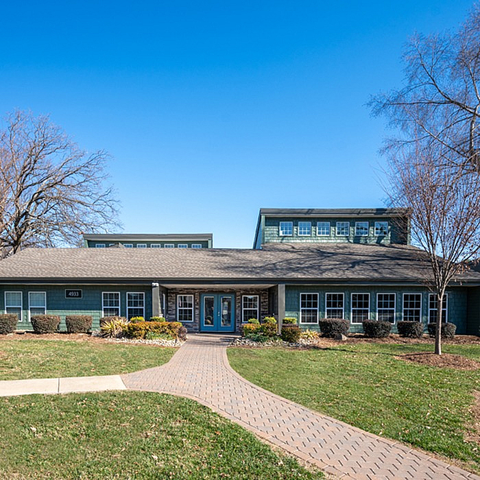 Charming apartment building with a welcoming entrance, surrounded by lush greenery and clear blue skies, offering a perfect blend of nature and modern living.