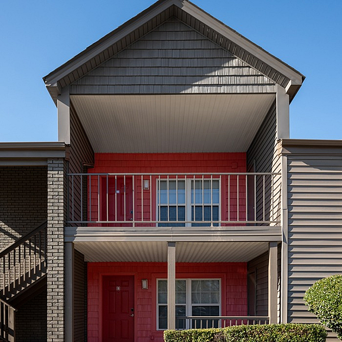 Charming two-story apartment exterior with vibrant red accents, private balconies, and inviting architectural design.