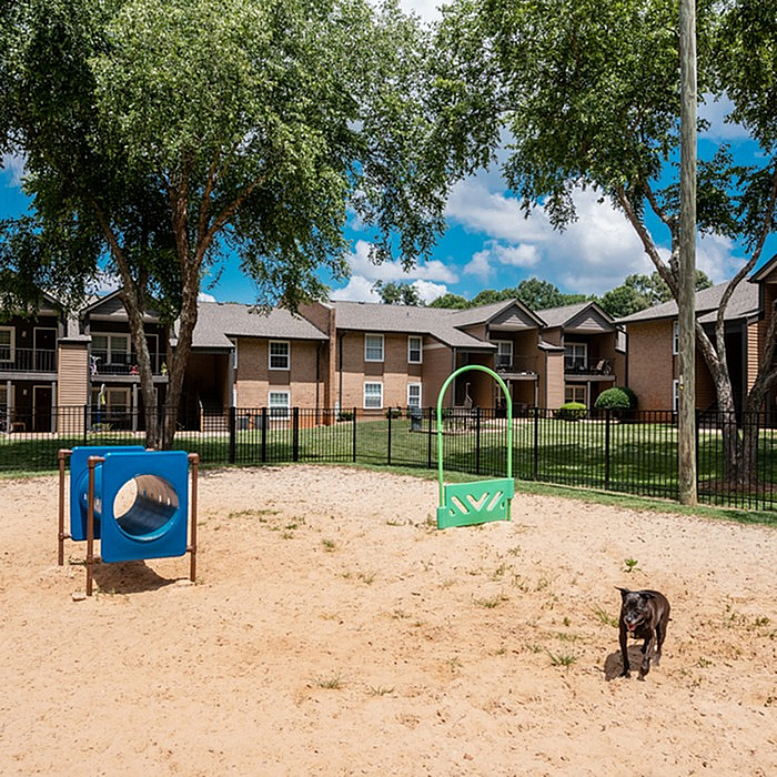 Charming apartment complex with a lush green landscape and a fun sandy playground, perfect for families and pet-friendly living.