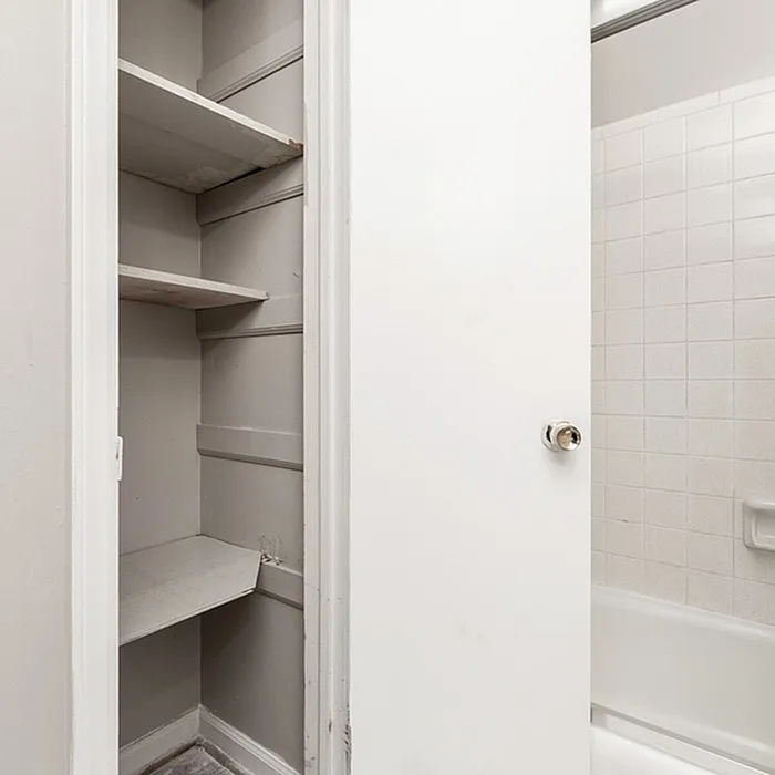 Bright and efficient bathroom setup featuring a built-in shelving unit and gleaming tiled bathtub, offering practicality and style.