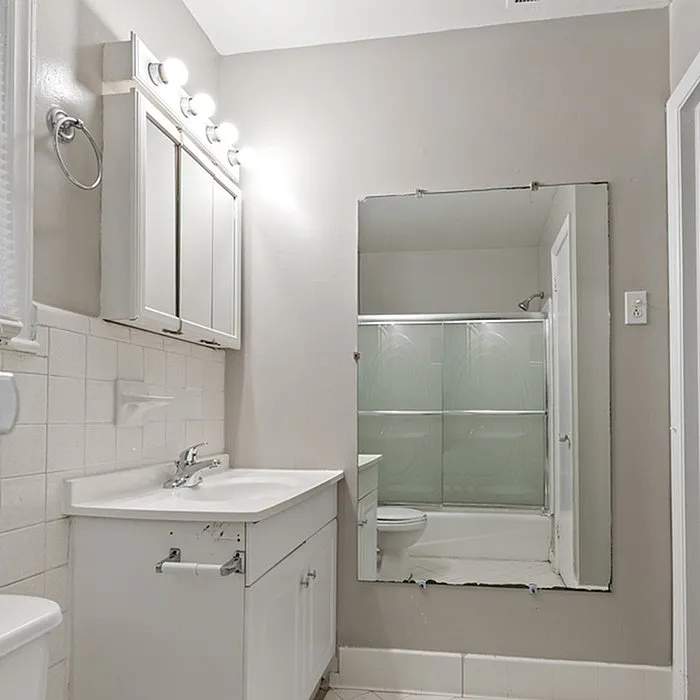 Elegant bathroom featuring sleek white cabinetry, a large mirror, and modern lighting fixtures, creating a bright and inviting space.