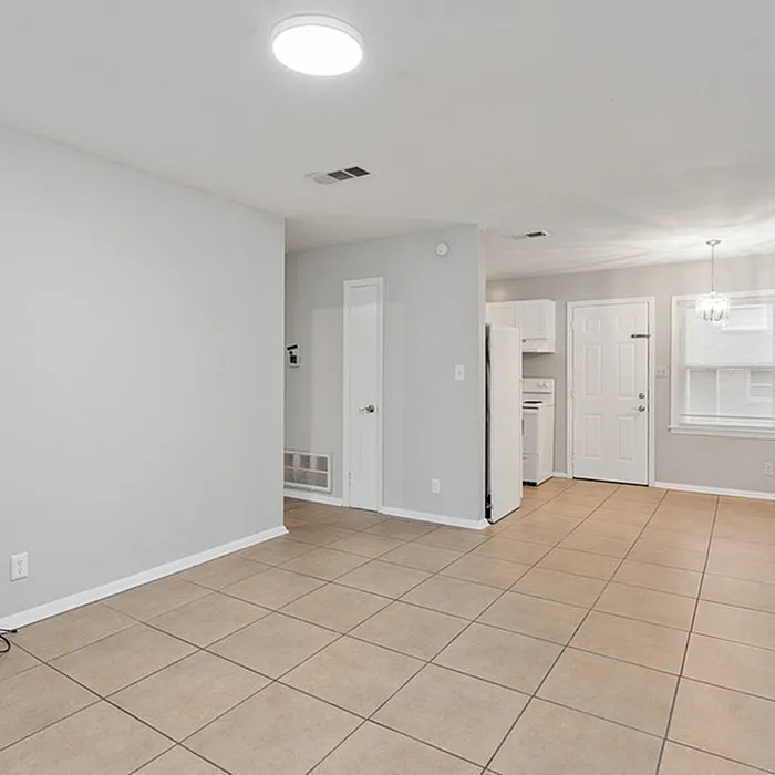 Bright open-concept living space with modern tiled flooring, leading to a cozy kitchen area with ample natural light.