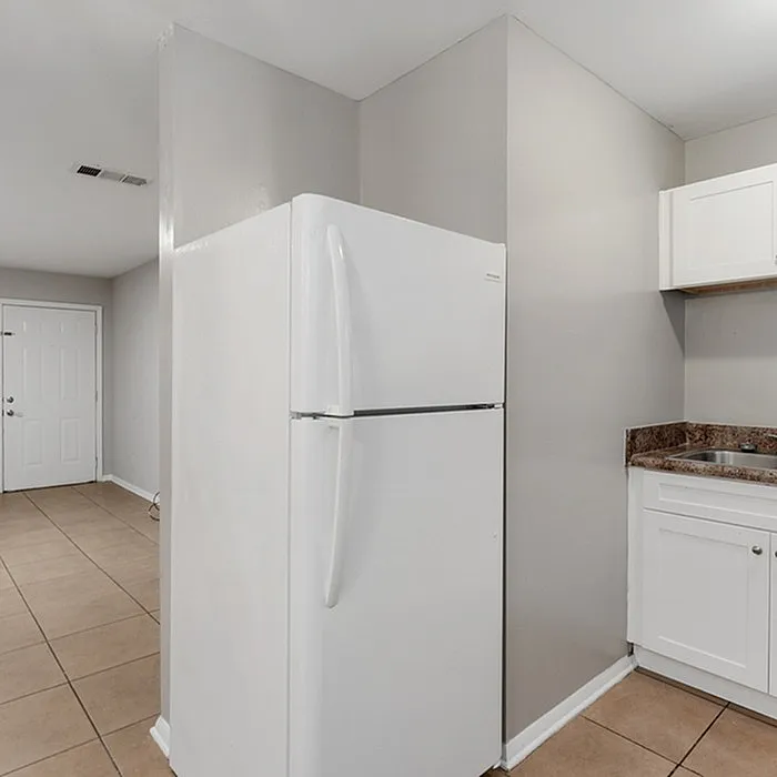 Bright kitchen with modern white refrigerator, sleek cabinetry, and elegant tiled flooring.
