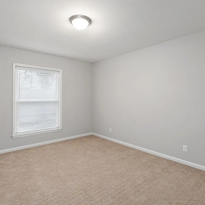 Bright and inviting room with soft carpet flooring, fresh gray walls, and ample natural light through a large window, perfect for a peaceful retreat.