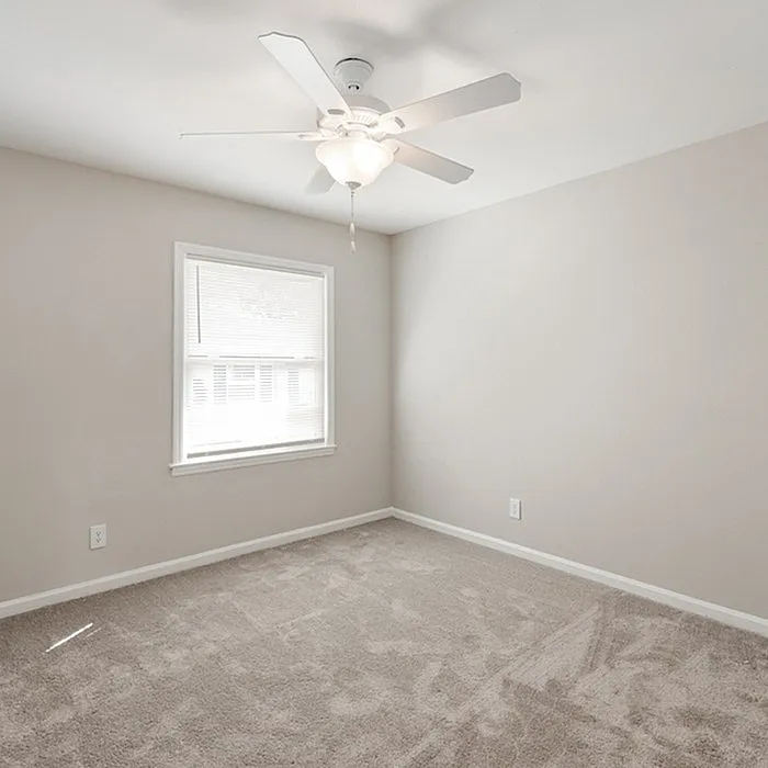 Bright and airy bedroom with plush carpeting, neutral walls, and a ceiling fan, offering a cozy and inviting atmosphere.