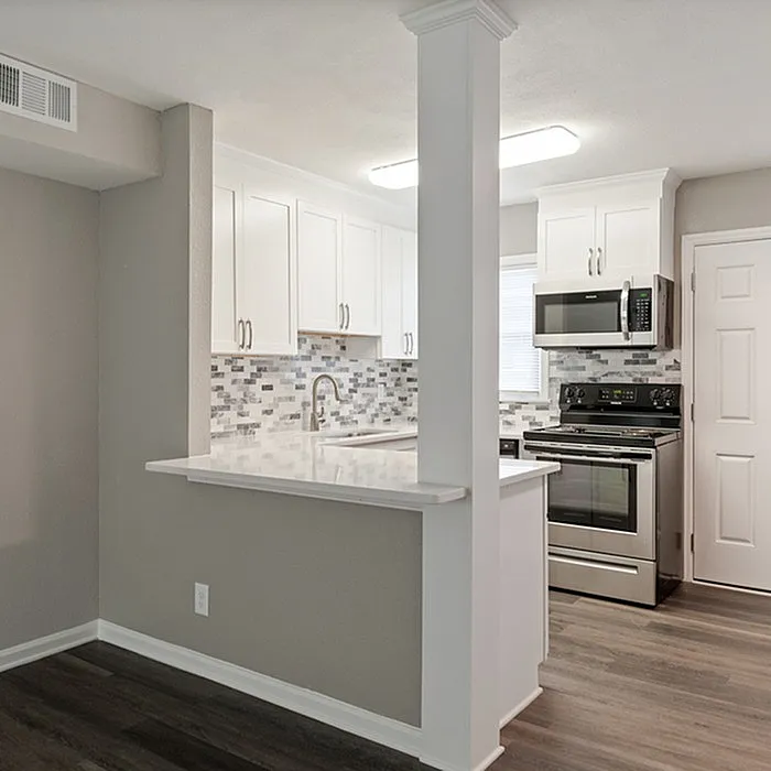 Modern apartment kitchen with sleek white cabinets, stylish backsplash, and stainless steel appliances.