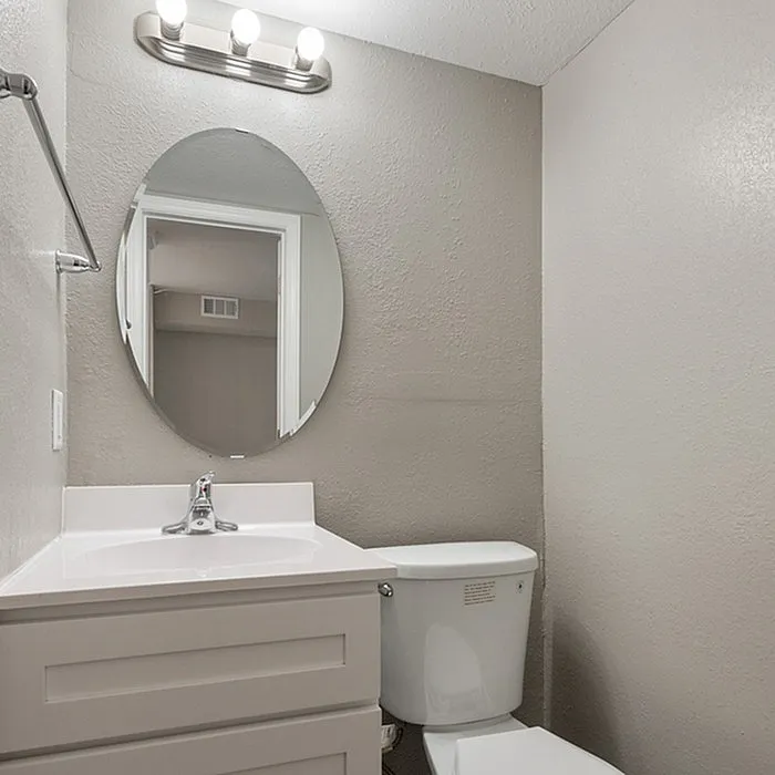 Modern bathroom featuring sleek white vanity with an oval mirror, elegant lighting, and contemporary finishes.