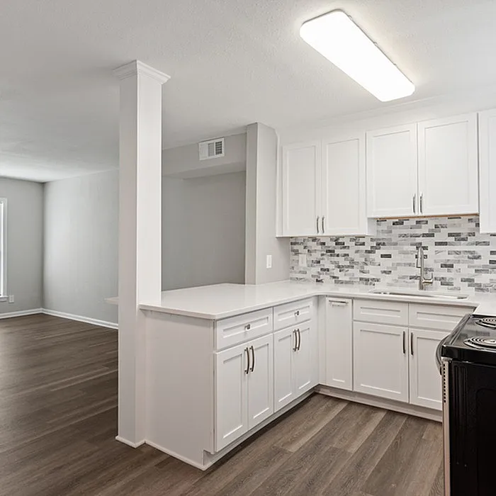 Modern kitchen with sleek white cabinetry and stylish backsplash, opening into a spacious living area with elegant wood flooring.