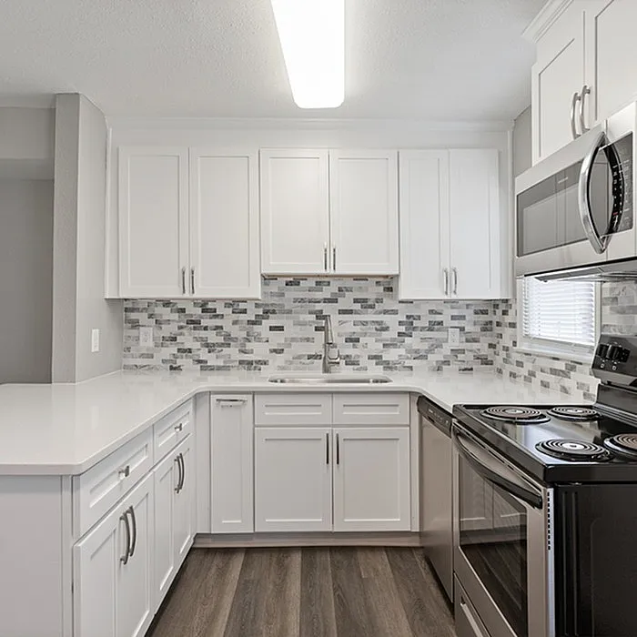 Bright and modern kitchen with sleek white cabinetry, stylish mosaic backsplash, and stainless steel appliances.