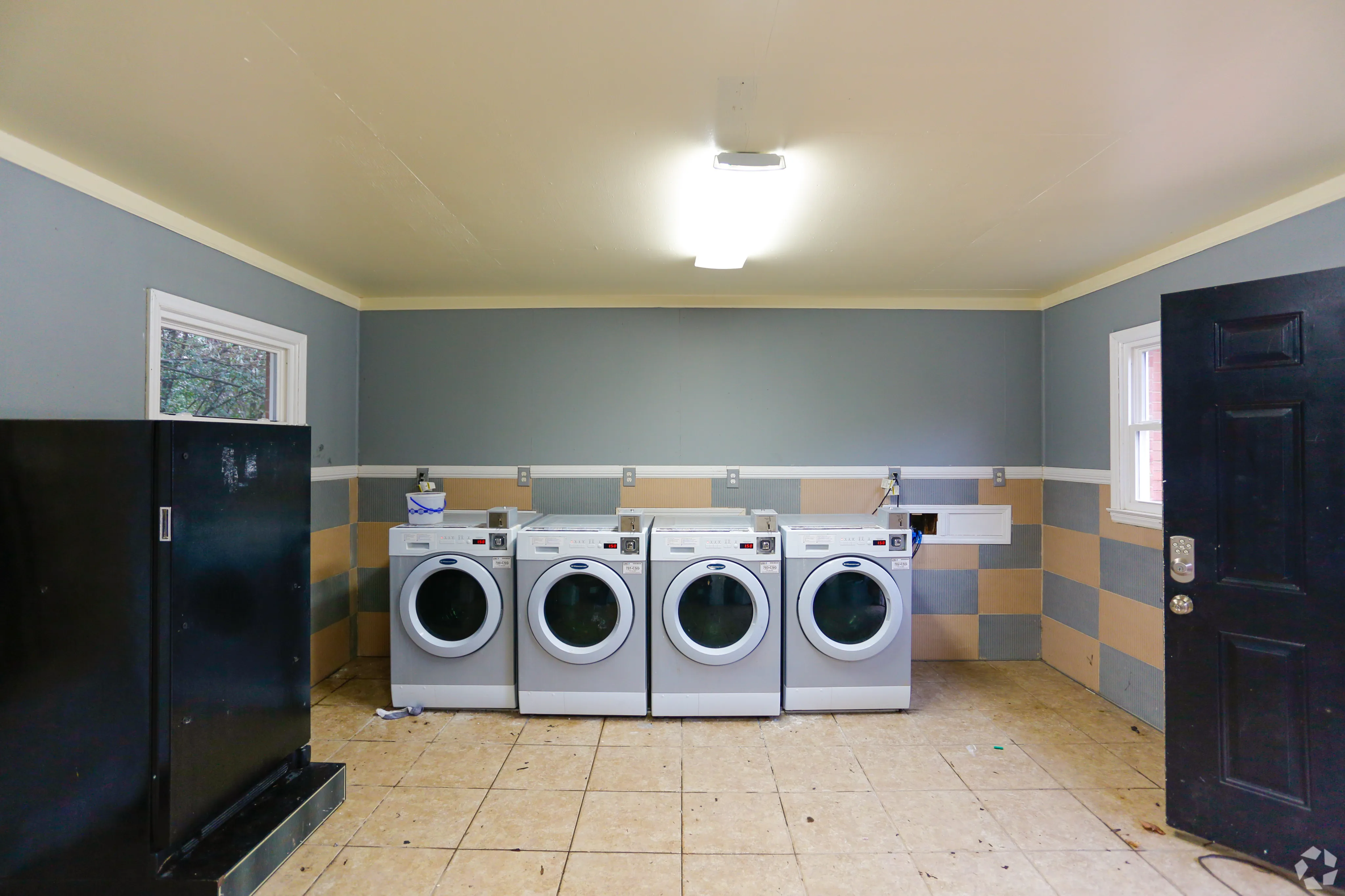 Inviting and spacious laundry room featuring four sleek, modern washing machines, complemented by a stylish striped wall design and practical tiled flooring.