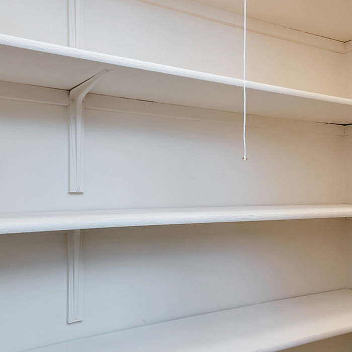 Spacious built-in shelving unit in a bright room with a pull string light, perfect for stylish storage solutions.