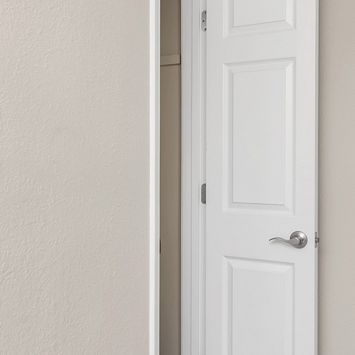 Sleek white interior door with modern handle, opening to reveal a cozy closet space, perfect for organized living.