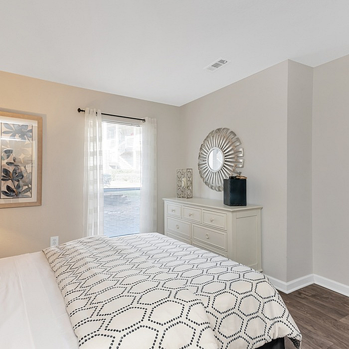 Inviting bedroom with stylish decor, featuring a plush bed, elegant dresser, and bright natural lighting through a large window.