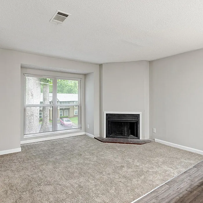 Bright and airy living room with a large window, cozy fireplace, and plush carpet flooring.