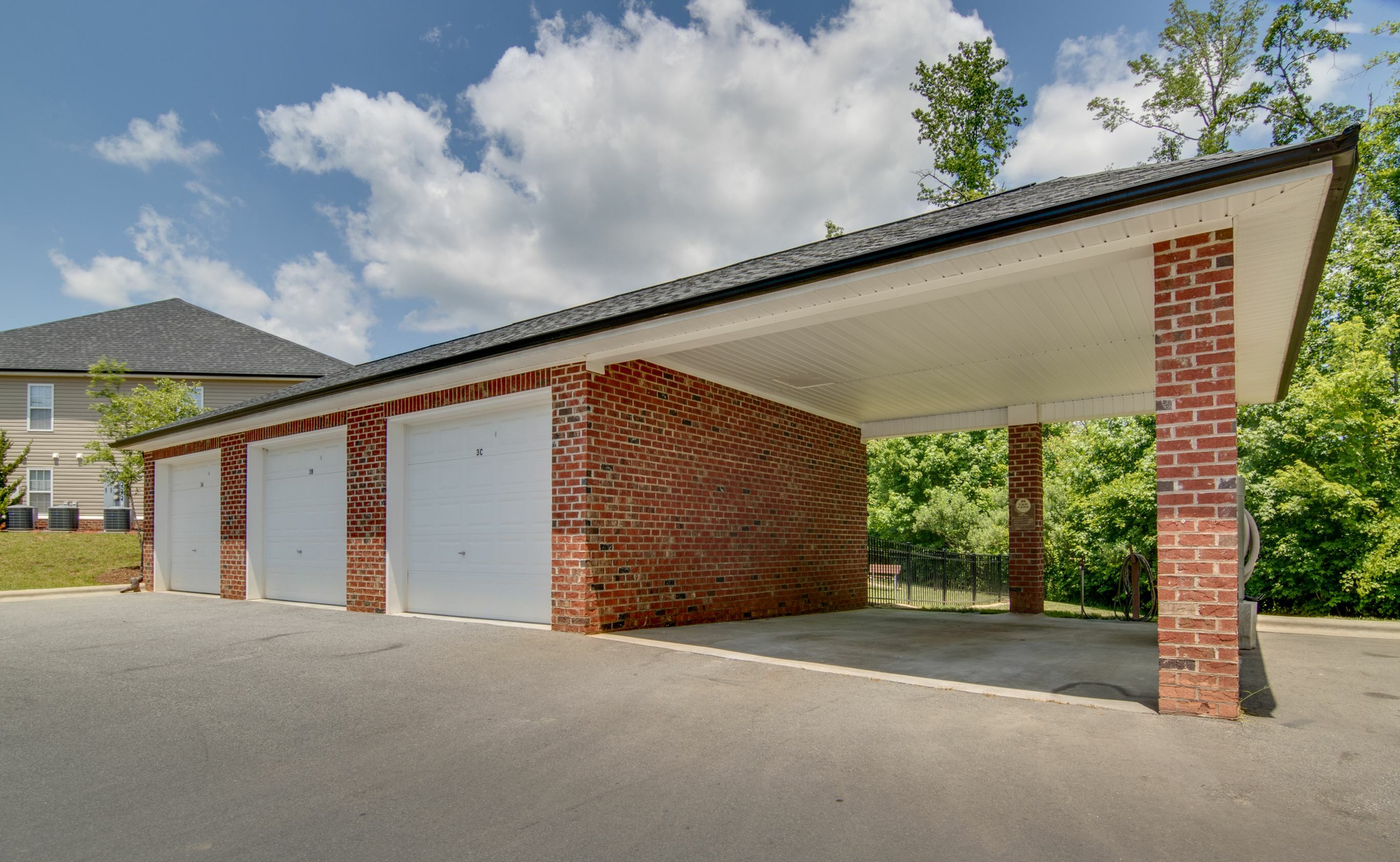 Charming brick garage with multiple doors and a covered area set against a backdrop of lush greenery and a clear blue sky.