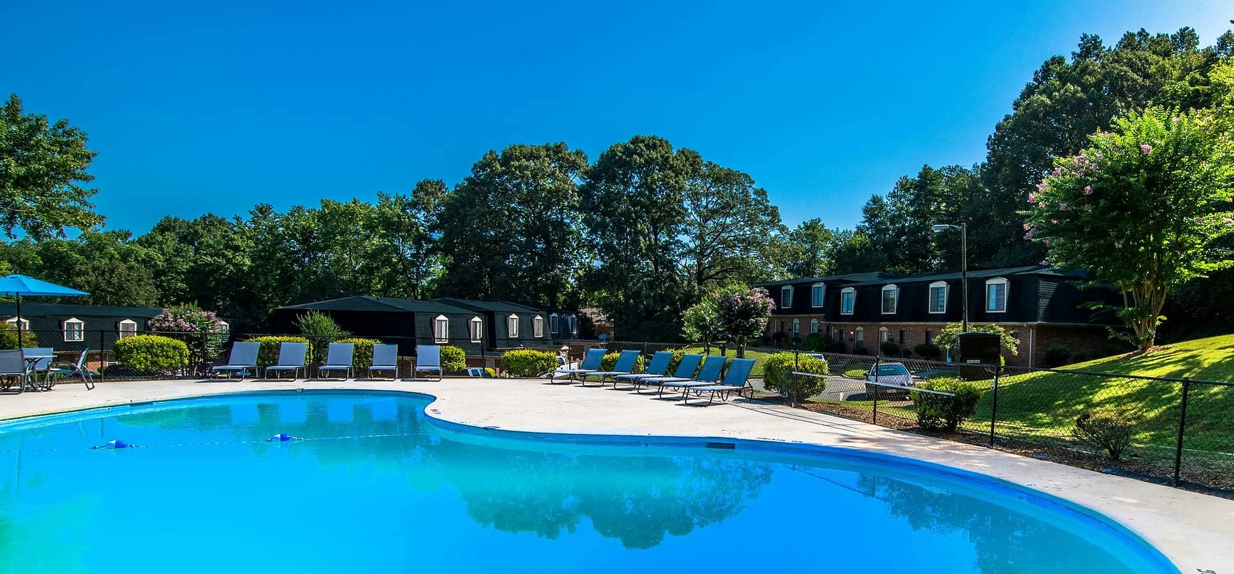 Inviting apartment complex with a sparkling swimming pool, surrounded by lush greenery and sun loungers for a perfect relaxation spot.