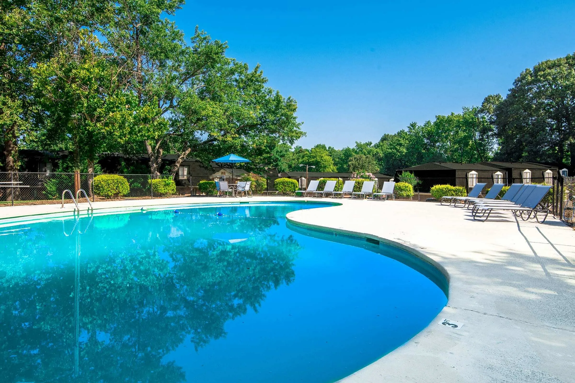 Refreshing outdoor pool area surrounded by lush greenery, featuring comfortable lounge chairs and shaded dining space.