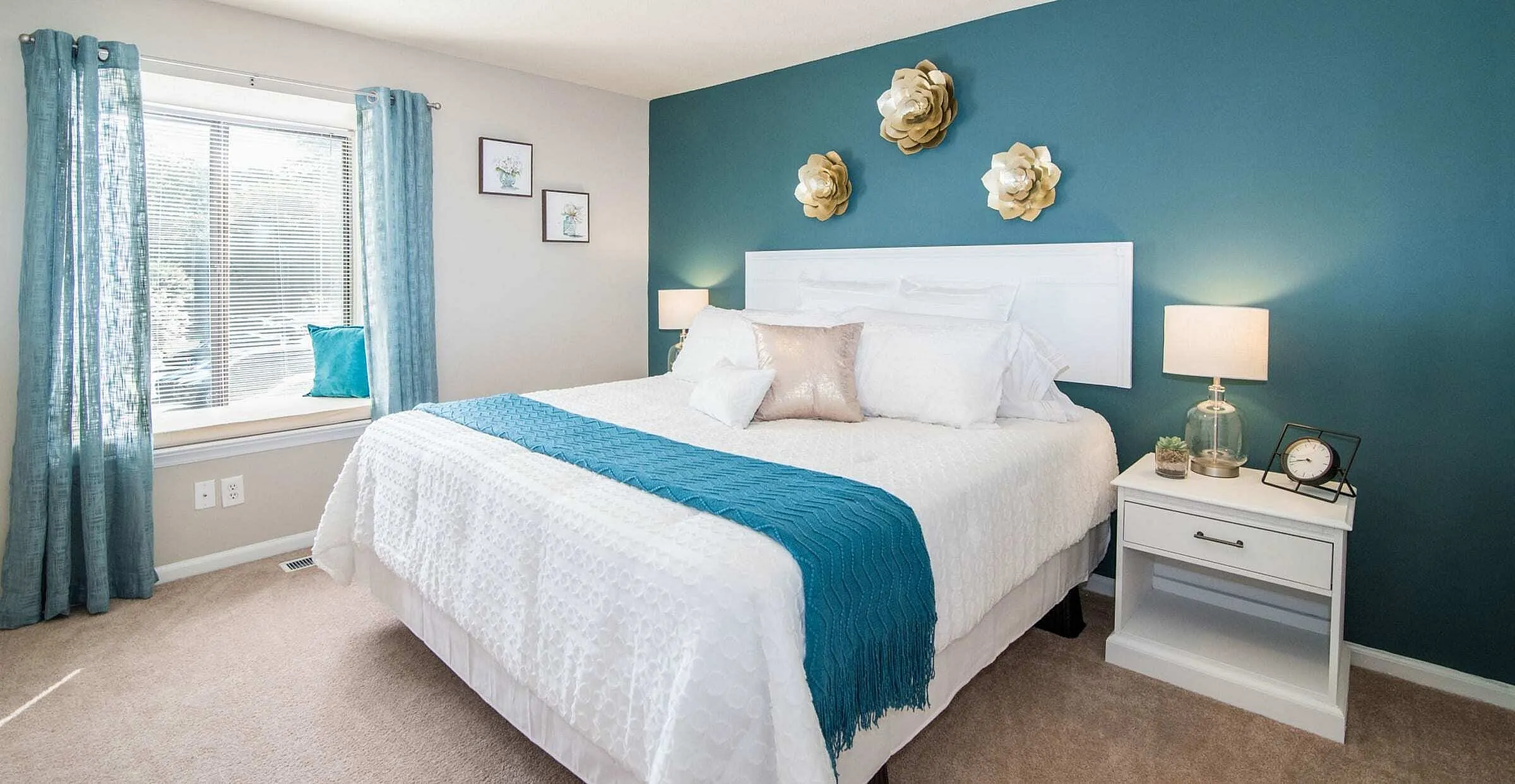 Elegant bedroom with plush bedding, teal accents, and contemporary decor featuring golden wall flowers.