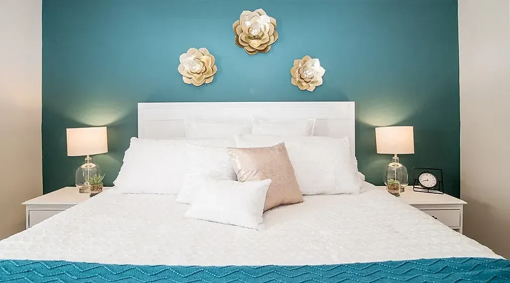 Elegant bedroom with plush bedding, teal accents, and contemporary decor featuring golden wall flowers.