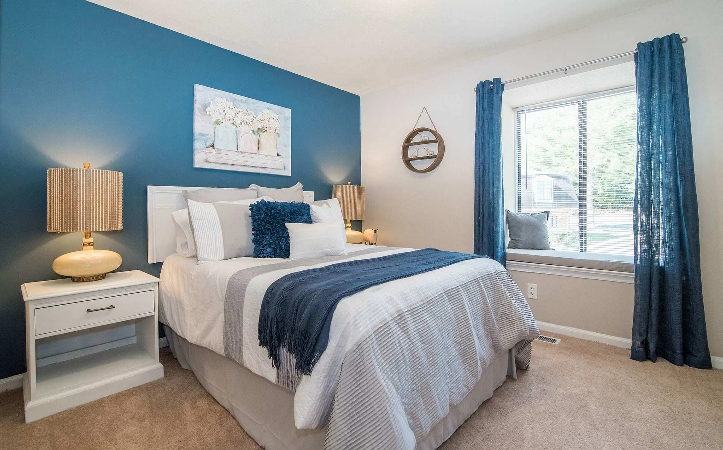 Cozy and elegant bedroom with a stylish blue accent wall, plush bedding, and inviting natural light through a large window.