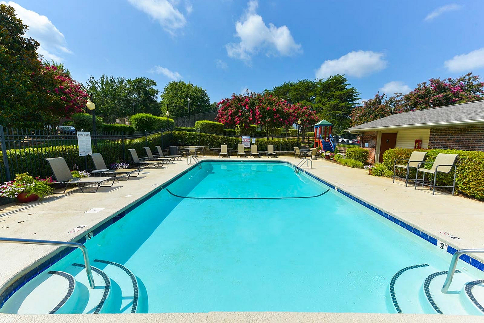 Inviting outdoor swimming pool with plush lounge chairs and vibrant landscaping under a clear blue sky, perfect for relaxation and leisure.