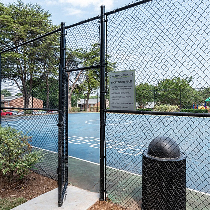 Inviting outdoor sports court with vibrant blue surface, fenced for safety, nestled within lush greenery.