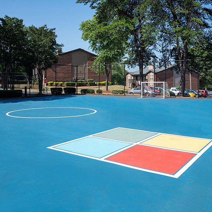 Vibrant outdoor recreational area with a bright blue sports court surrounded by lush greenery and modern apartment buildings, offering a perfect blend of active living and serene environment.