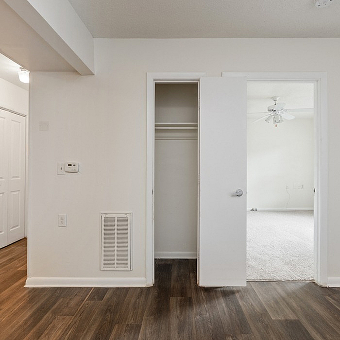 Inviting apartment showcasing a walk-in closet, elegant wooden flooring, and a light-filled room with ceiling fan in the background.