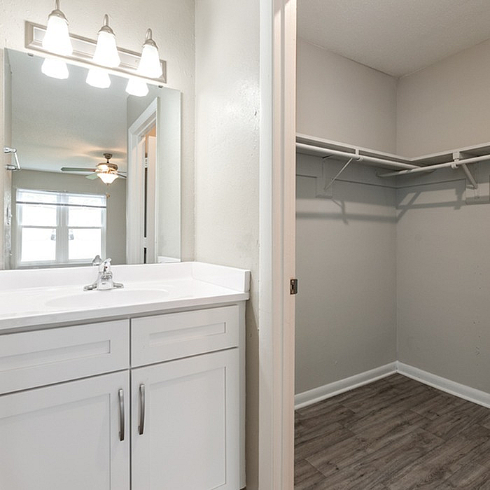 Bright bathroom with a sleek white vanity and a spacious walk-in closet, featuring elegant lighting and modern finishes.