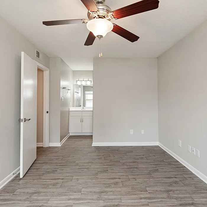 Elegant bedroom with sleek laminate flooring, ceiling fan, and an en-suite vanity showcasing modern living.