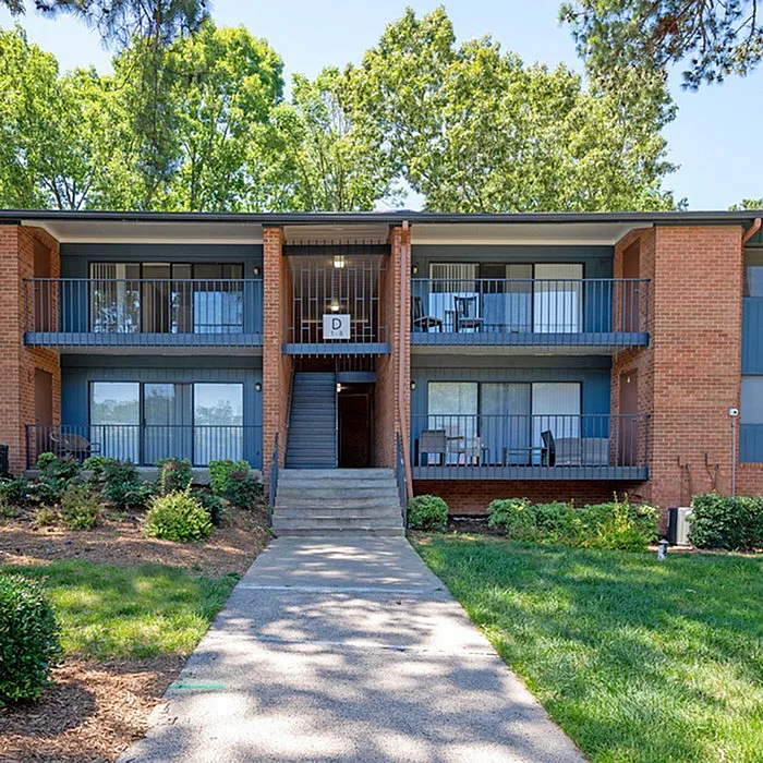 Charming brick apartment building surrounded by lush greenery, featuring spacious balconies perfect for relaxation.