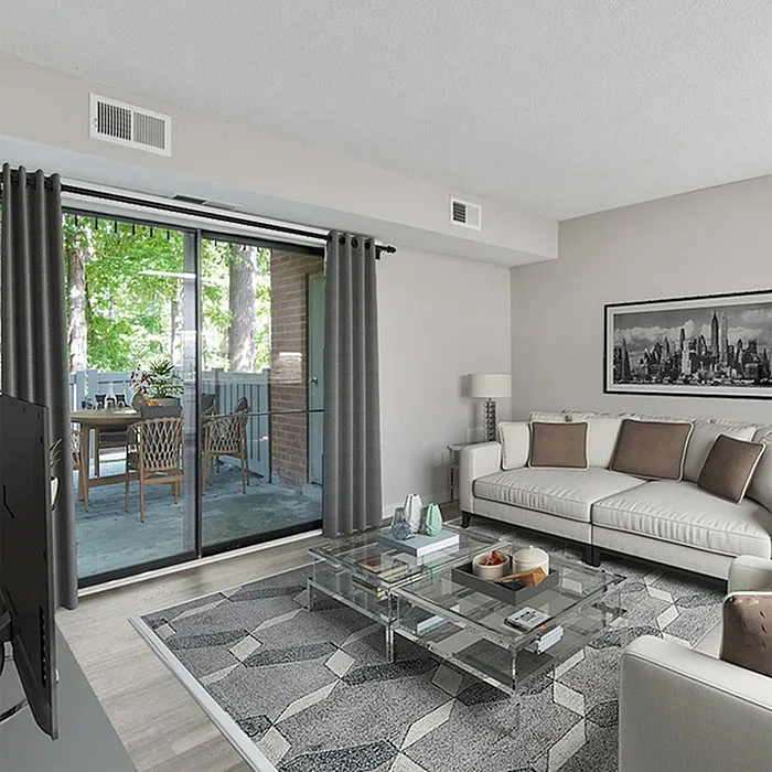Bright and modern living room with plush sofa, glass coffee table, and sliding glass doors leading to a scenic balcony with outdoor seating.