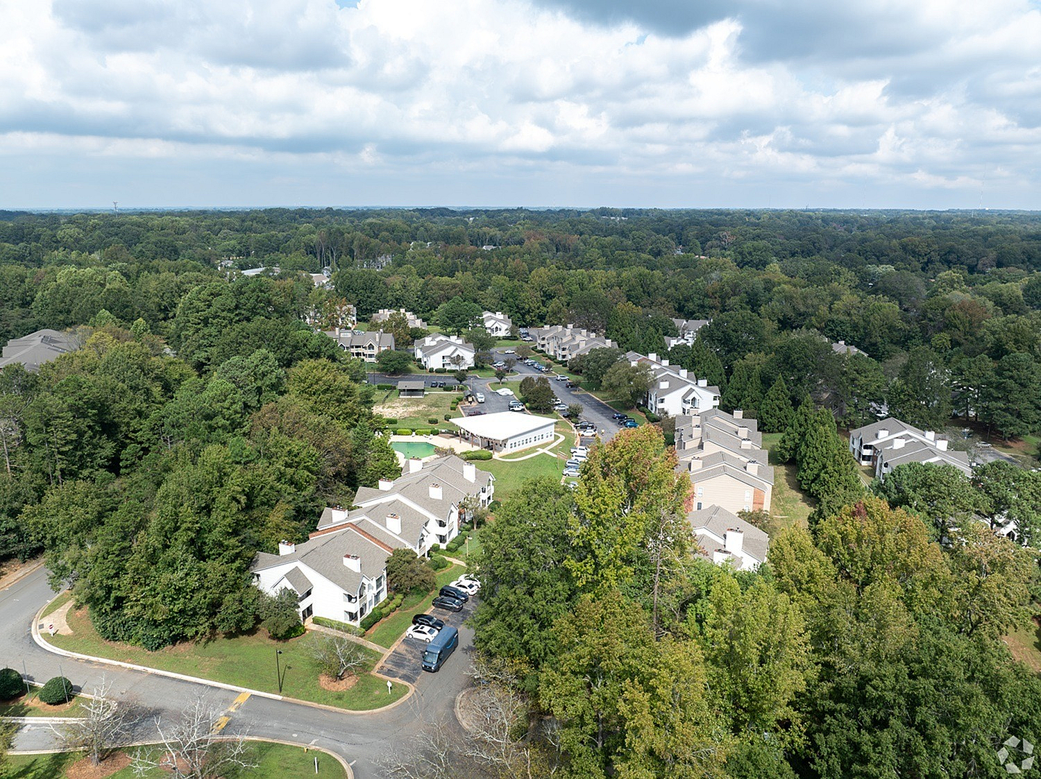 Charming aerial view of a serene neighborhood nestled within lush green surroundings, showcasing modern apartments and tree-lined streets for an idyllic living experience.