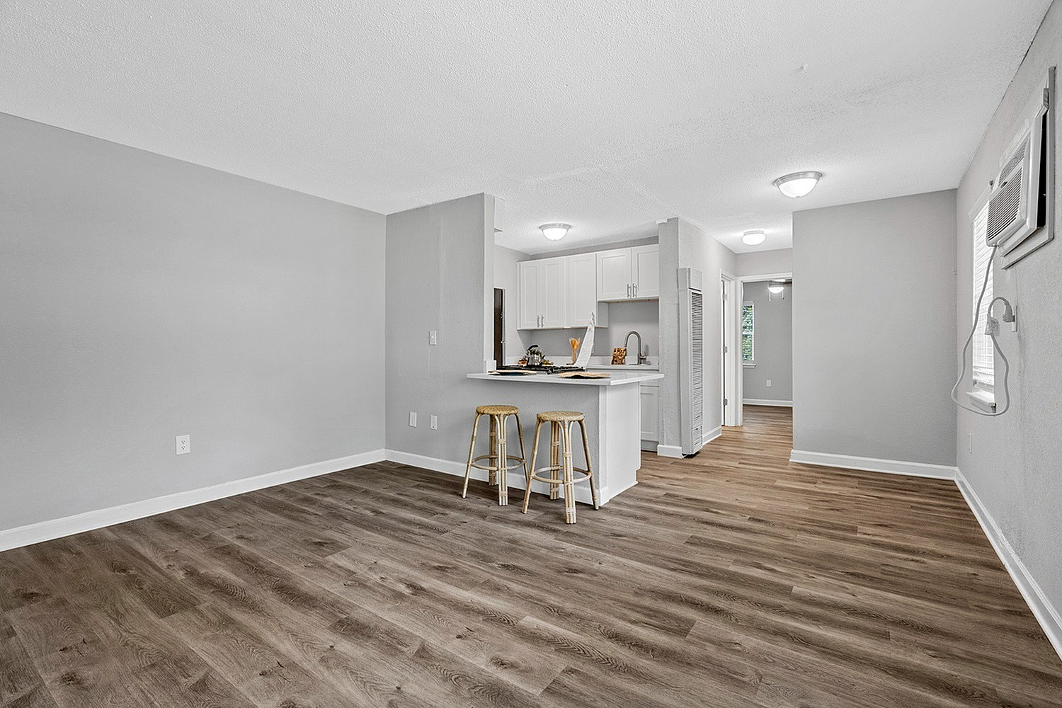 Modern apartment interior with stylish hardwood flooring, a cozy breakfast bar with stools, and an open-plan kitchen featuring sleek white cabinetry.