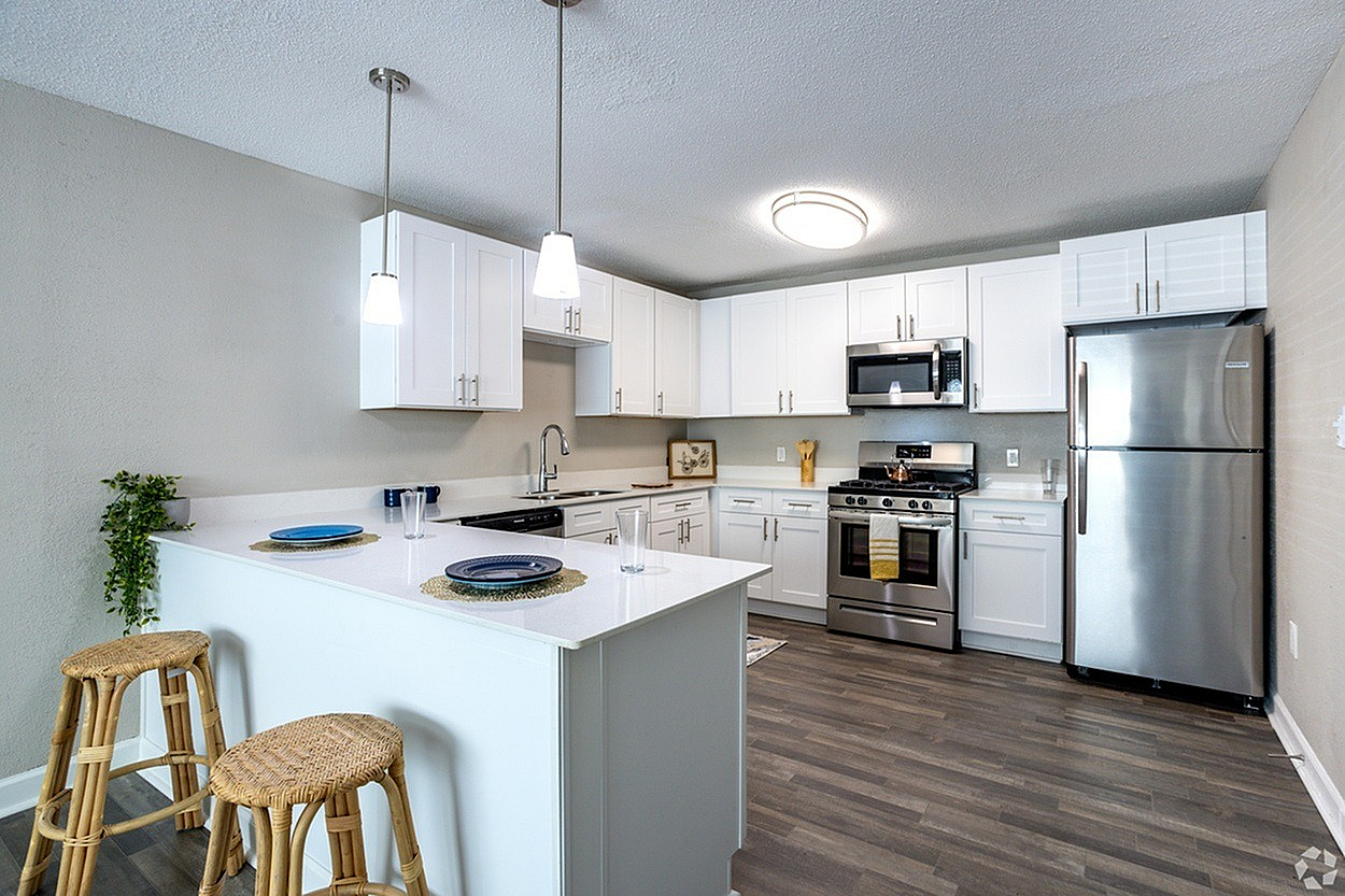 Modern kitchen with sleek white cabinets, stainless steel appliances, and stylish breakfast bar with woven stools.