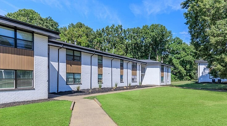 Charming apartment complex with a modern exterior, surrounded by lush greenery and bright blue skies.