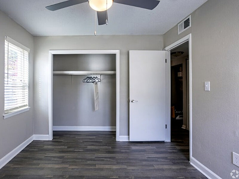 Bright and spacious bedroom with elegant wooden flooring, large closet, and modern ceiling fan, perfect for a cozy living experience.