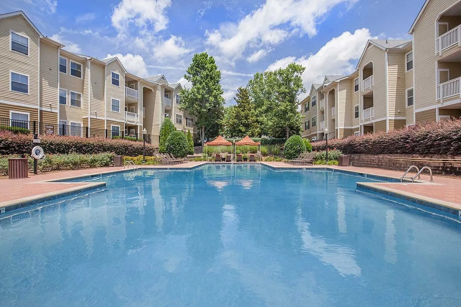 Luxurious apartment complex with a sparkling blue pool and inviting lounge areas, surrounded by lush landscaping and modern architecture.