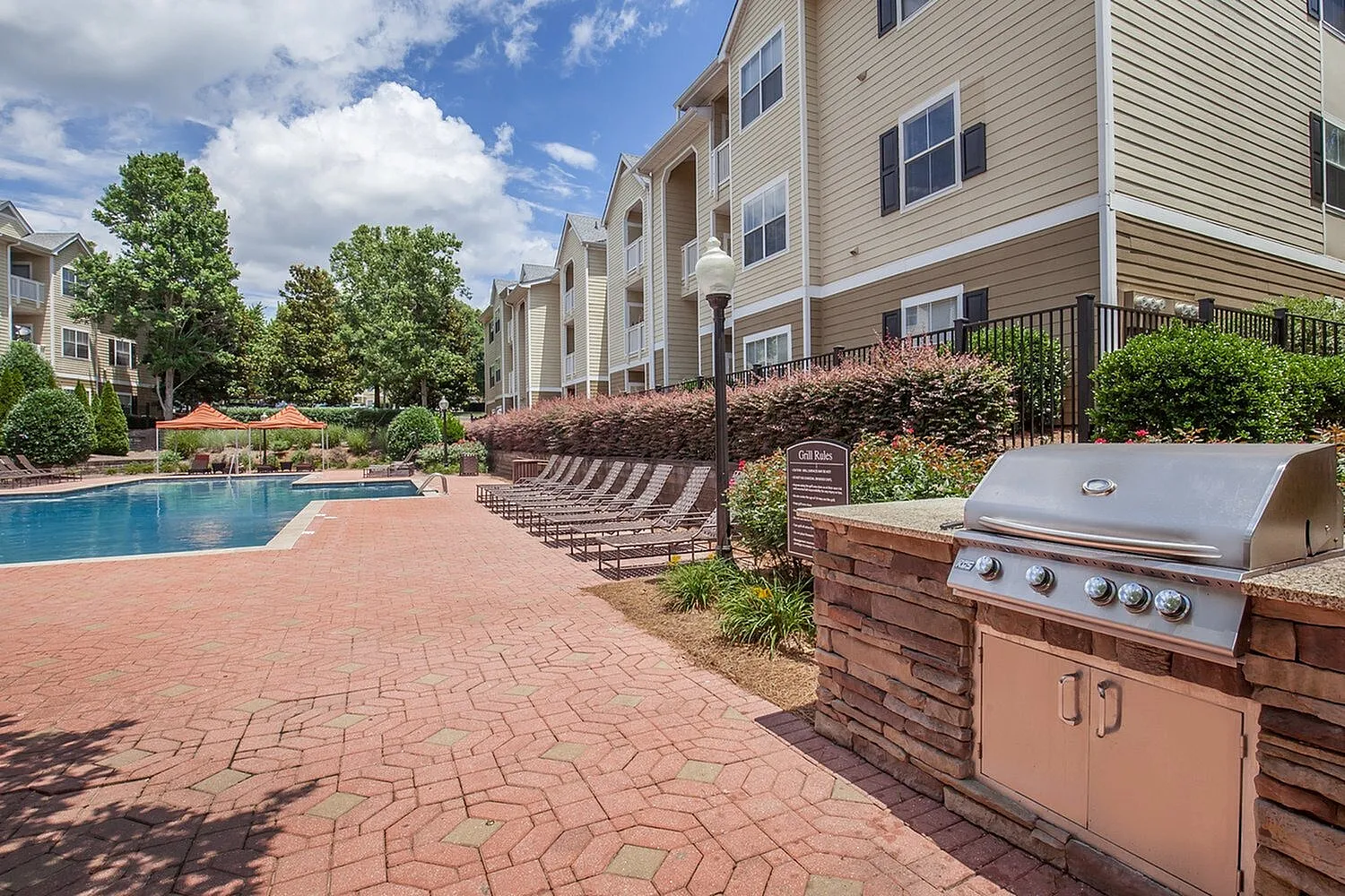 Luxurious apartment community featuring a sparkling swimming pool, modern outdoor grill, and inviting lounge area surrounded by lush greenery.